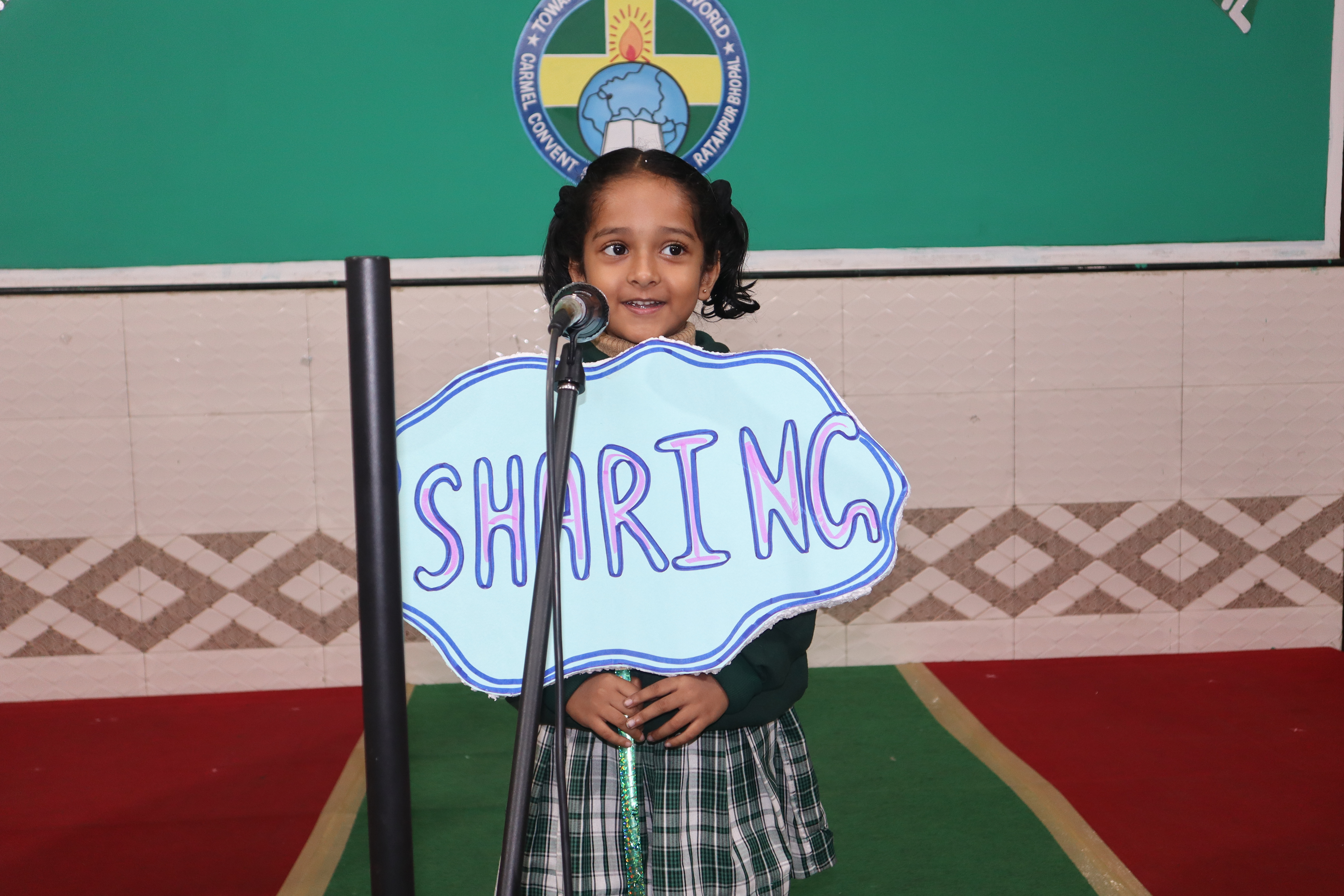 A child at the microphone holding a hand made placard that reads Sharing