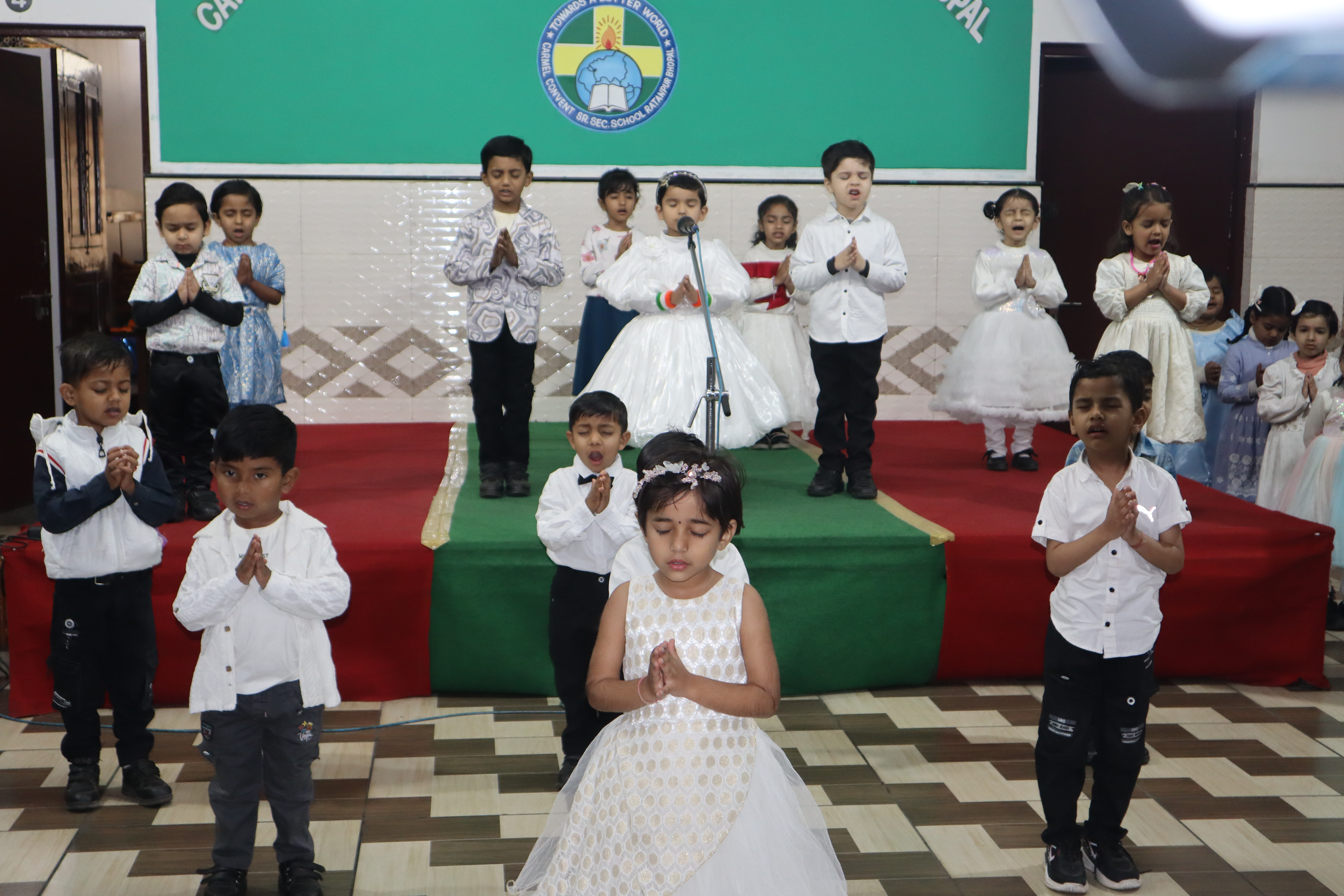 Children dressed in white singing a prayer song on stage